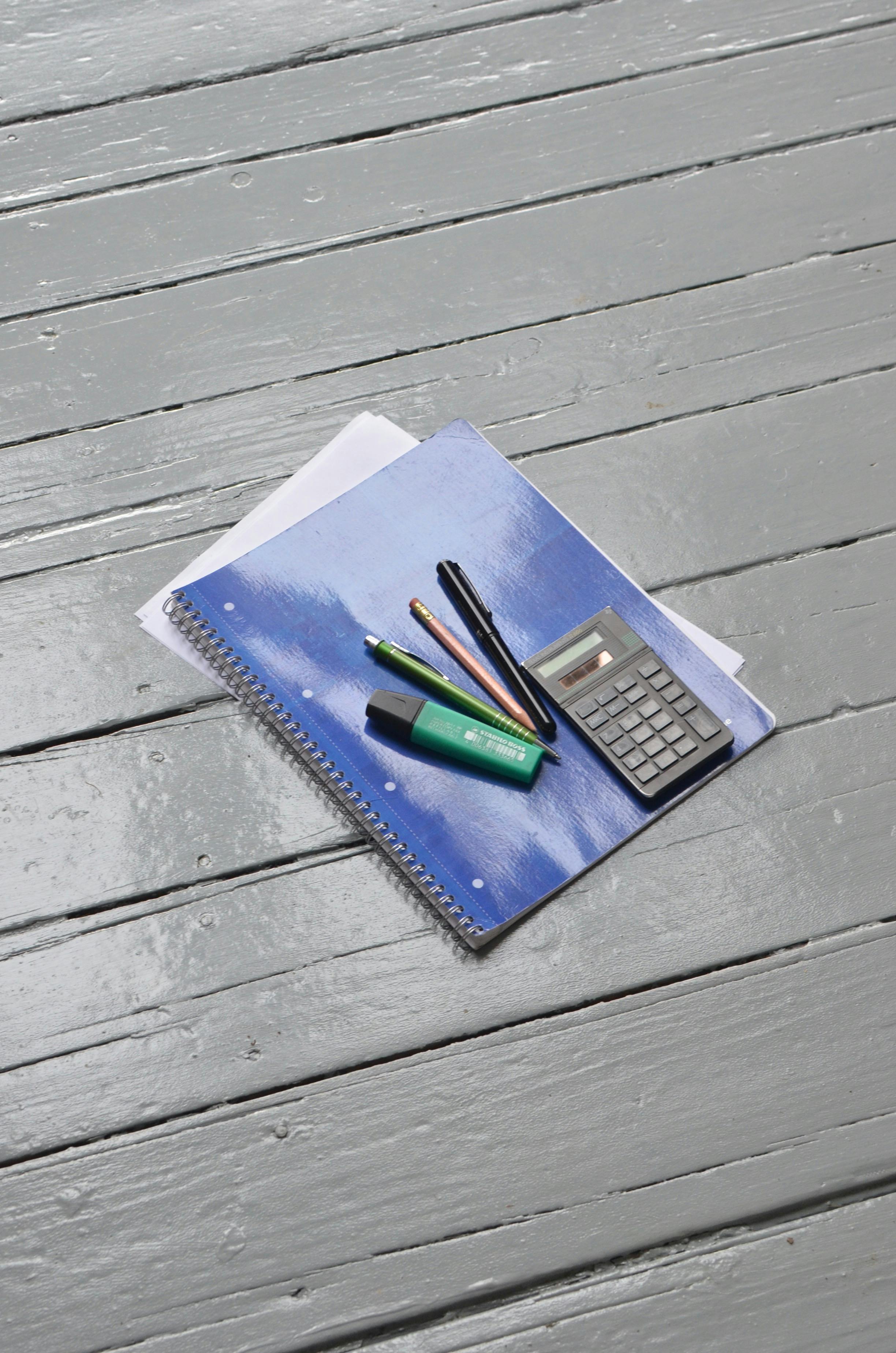 pen pencils and calculator placed on notebook