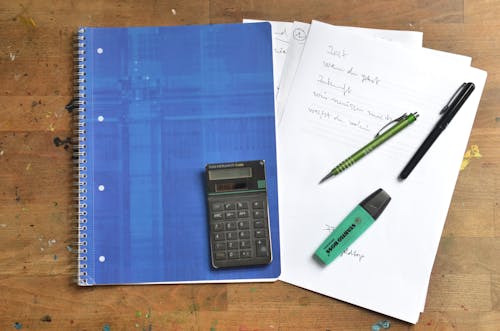 Free From above of blue notebook papers calculator marker and pens on wooden office table Stock Photo