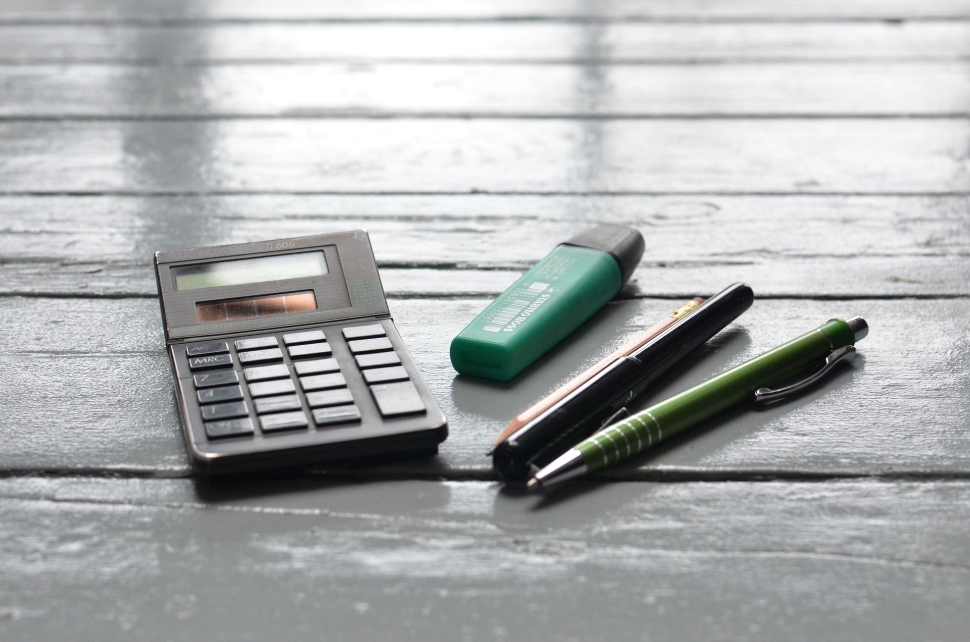 Une calculatrice et des stylos posés sur un bureau en bois.