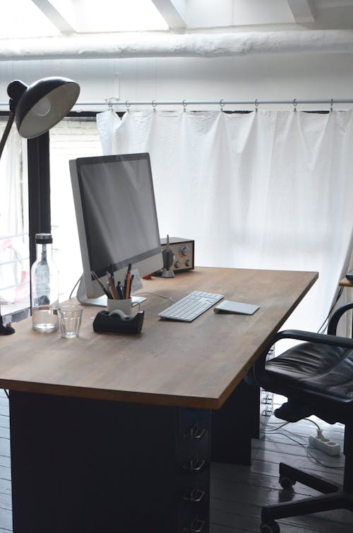 Office table with big monitor keyboard lamp and stationeries and chair in modern workplace