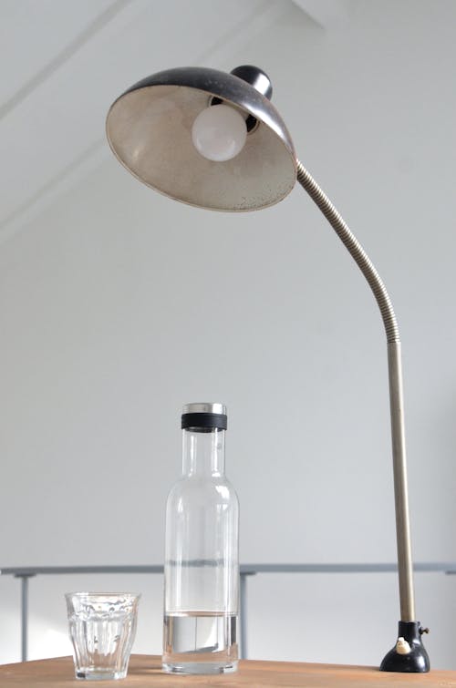 Free Modern metal switched off lamp placed on table near bottle of water and small glass in light room Stock Photo
