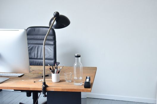 Modern minimalistic workplace with contemporary laptop placed on wooden table with bottle of water and lamp with big leather chair