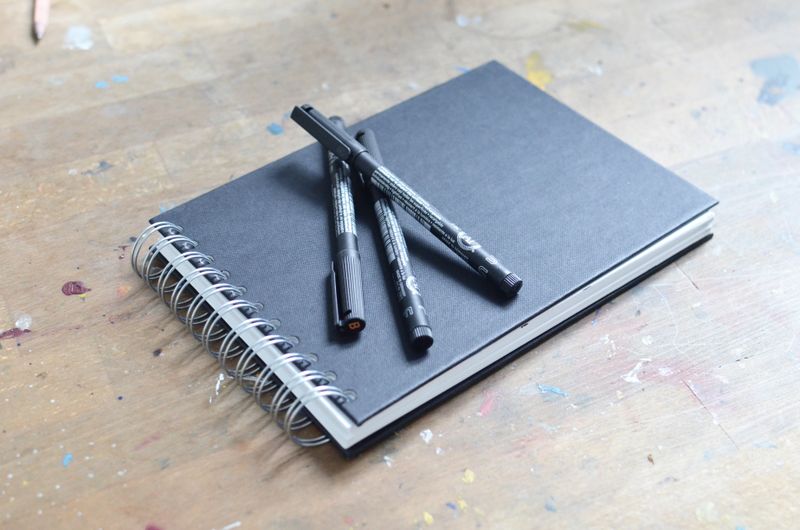 Fineliners resting on a spiral sketchbook on a paint-marked bench — photo by Skylar Kang on Pexels