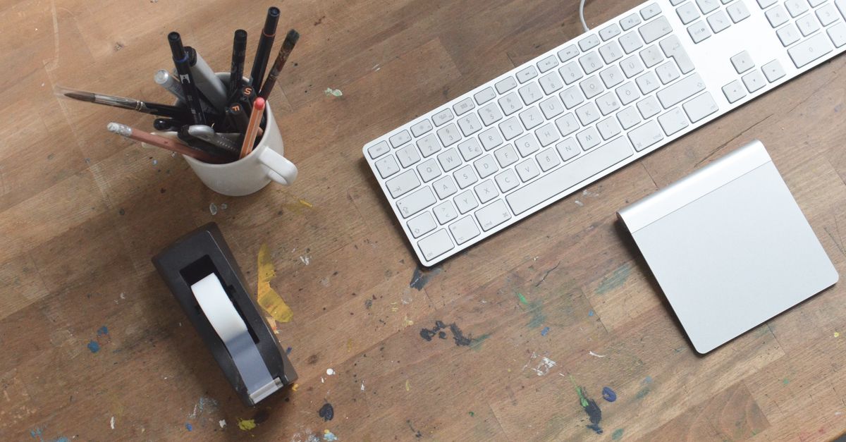 From above of artist workplace with modern keyboard and stationary placed on wooden desk stained with paint