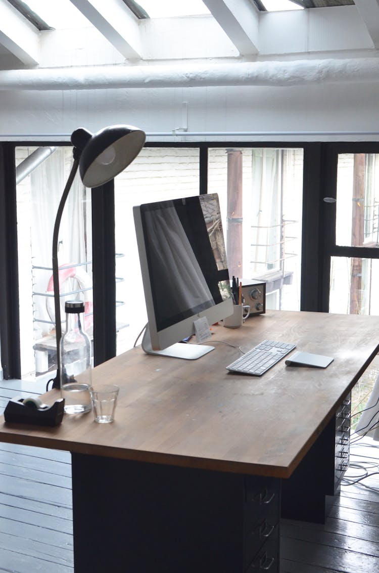 Modern Computer Placed On Desk With Lamp And Radio In Office