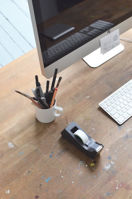 Stationery in mug near monitor on table