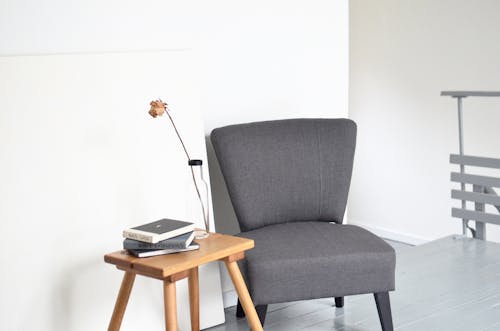 Armchair placed near wooden table with flower vase and books