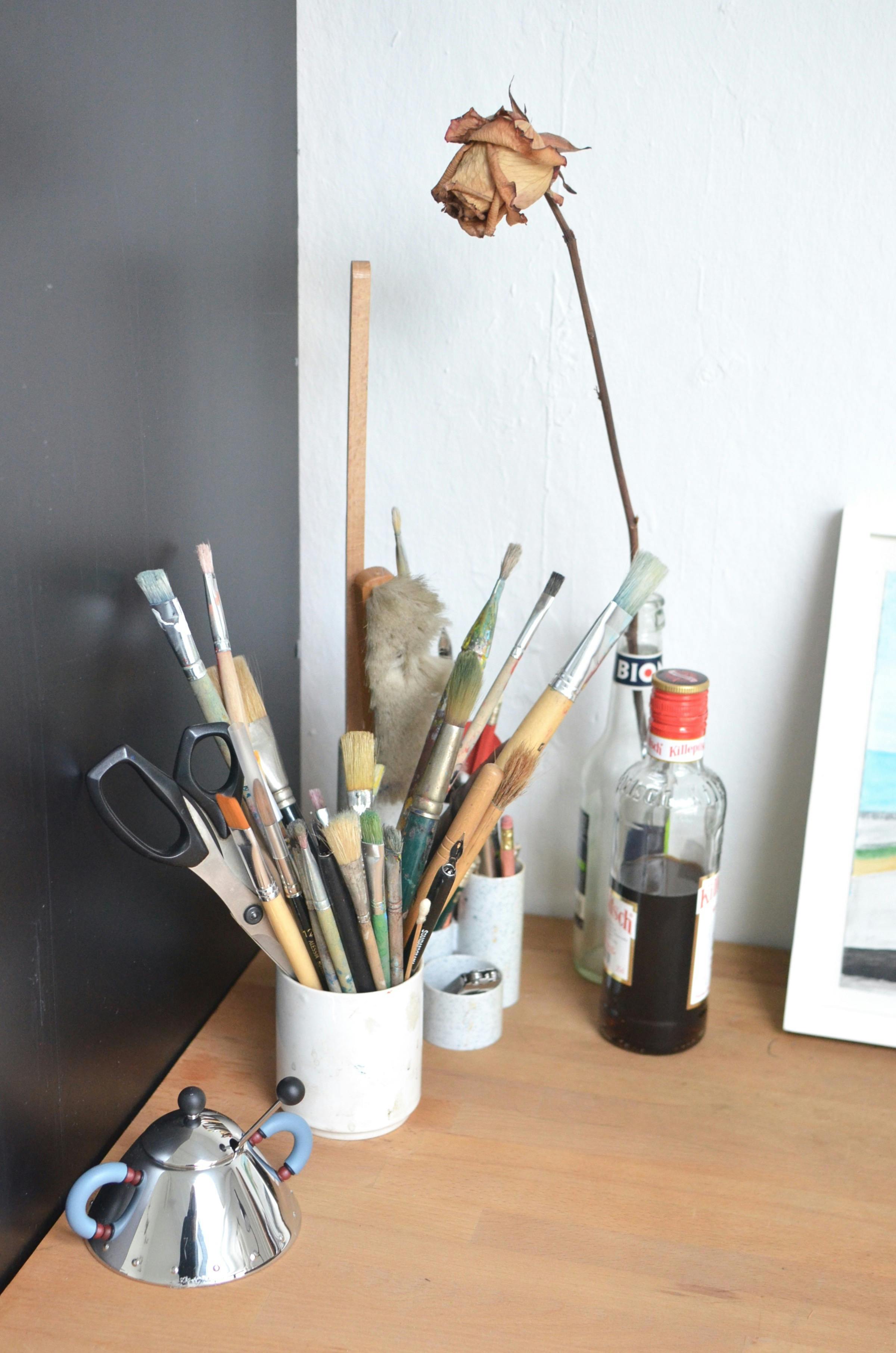 collection of paintbrushes and stationery placed on wooden desk in workshop