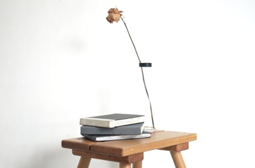 Stack of notebooks and vase with dry rose placed on wooden table