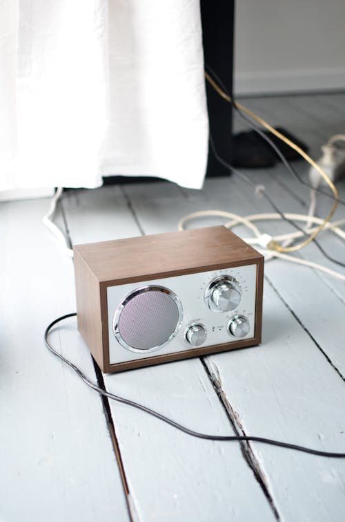 From above of vintage radio receiver with wooden case and chrome details placed on white timber floor and connected with wire