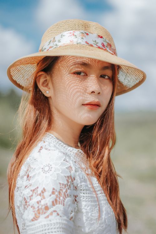 Free Side view of serene ethnic female in stylish hat and dress standing in sunny day Stock Photo
