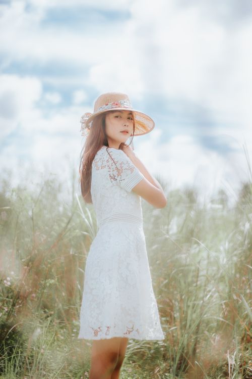 Free Side view low angle of Asian female in summer dress standing among grass meadow and looking at camera Stock Photo