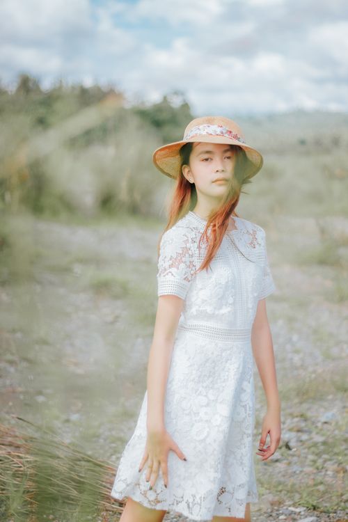 Free Tender Asian female with flying hair in dress standing on lawn with tall grass Stock Photo