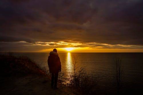 Schattenbild Des Mannes, Der An Der Küste Während Des Sonnenuntergangs Steht