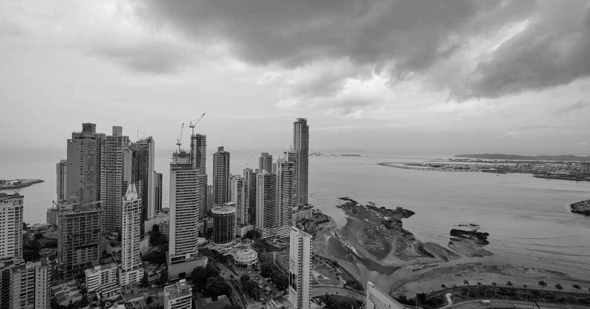 Vista aérea do moderno horizonte da Cidade do Panamá sob um céu nublado, com arranha-céus e costa.