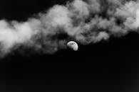 Black and white of shining moon on dark gloomy sky with clouds of smoke