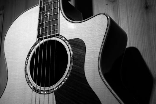 A detailed black and white close-up of a classic acoustic guitar, highlighting its strings and wood texture.