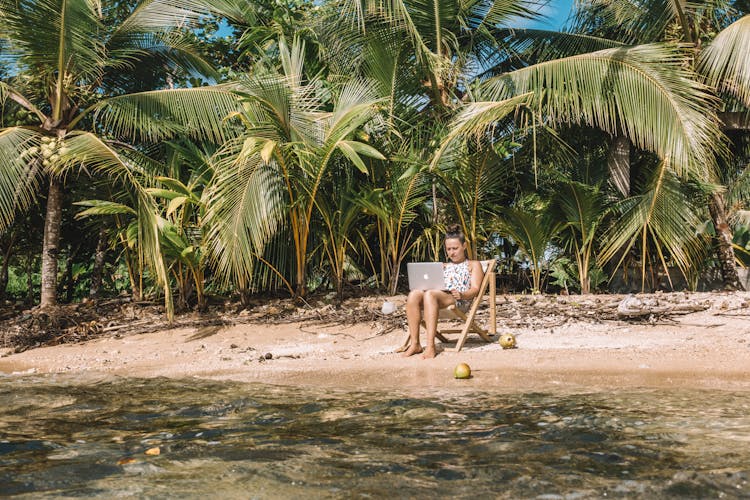 A Woman Working On The Beach While Sitting On A Wooden Chair