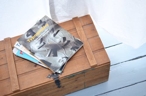 Free From above of various colorful journals placed on top of low vintage wooden box near white curtain in light room Stock Photo