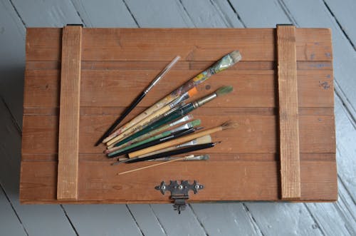 From above of various brushes placed on old fashioned chest box made of wood on light blue floor