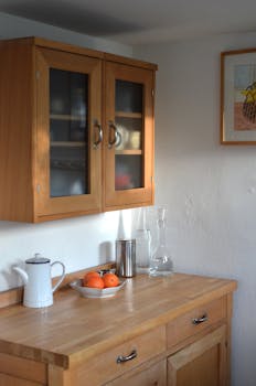 A minimalist kitchen featuring wooden cabinets, a wooden counter, and a bowl of oranges in natural daylight.