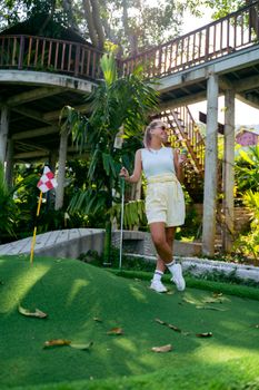 Young woman enjoying ice cream on a sunny mini golf course, with greenery and leisure vibe.