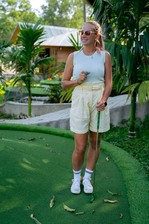 Free Smiling woman enjoying a game of mini golf outdoors on a sunny day. Stock Photo