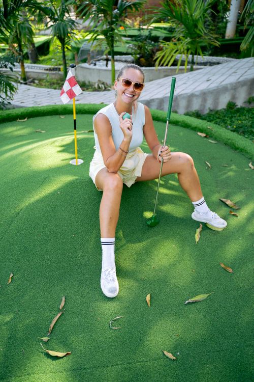 Free Smiling woman in sunglasses sitting on mini golf course with putter. Stock Photo