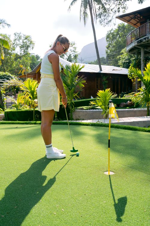 Free Woman enjoying mini golf on a lush green course at a tropical resort. Stock Photo