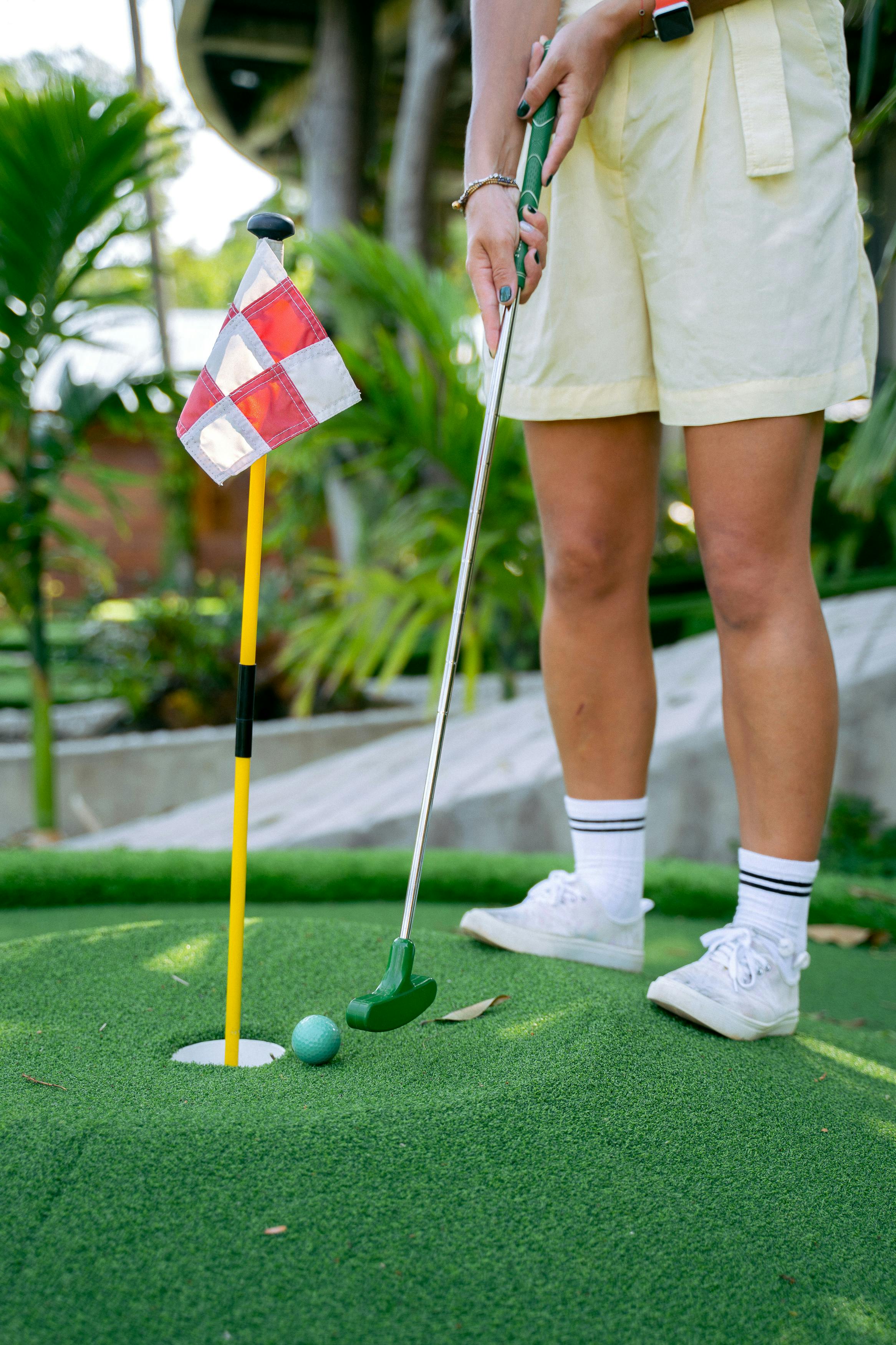 A person playing mini golf outdoors, focusing on a putt near the hole on a sunny day.
