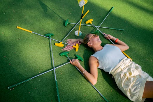 Woman lying joyfully on mini golf course surrounded by colorful putters.