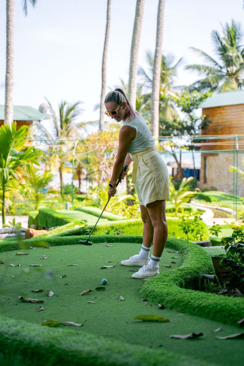 Free A woman playing mini golf in a tropical setting, focusing on her putting skills. Stock Photo