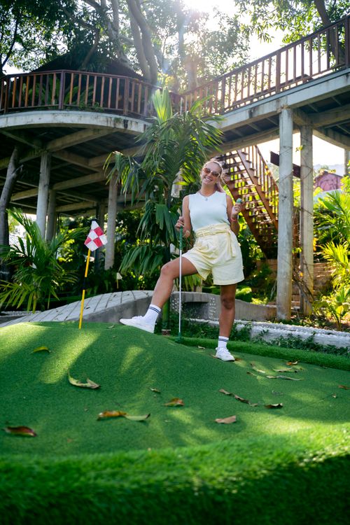 Free Cheerful woman playing mini golf outdoors, wearing casual attire and smiling. Stock Photo