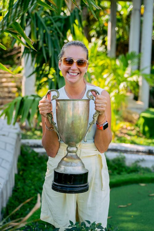 Free Celebrate victory with a joyful woman holding a trophy in a vibrant outdoor setting. Stock Photo