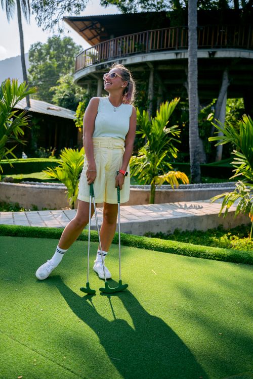 Free Smiling woman with putter on a sunny mini golf course, surrounded by lush greenery. Stock Photo