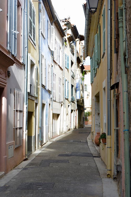 Paved narrow empty walkway between old small multicolored buildings in town at daylight in summer