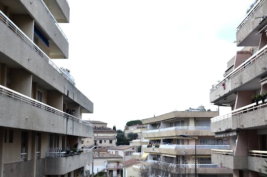 Exterior of houses with balconies with railings decorated with potted plants on street in town under bright sky in daylight