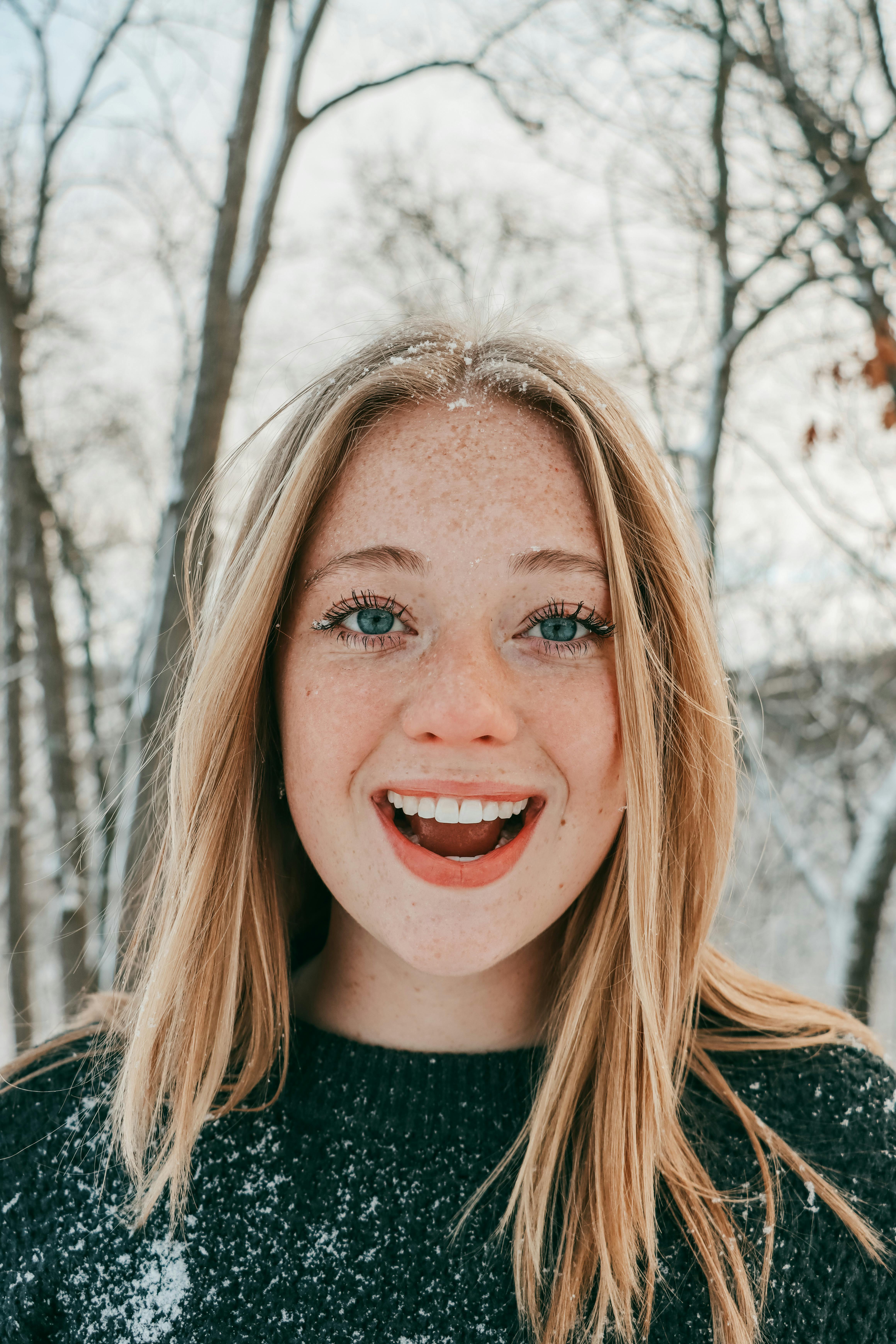 A joyful young woman with light brown hair smiles amidst a snowy outdoor scene.