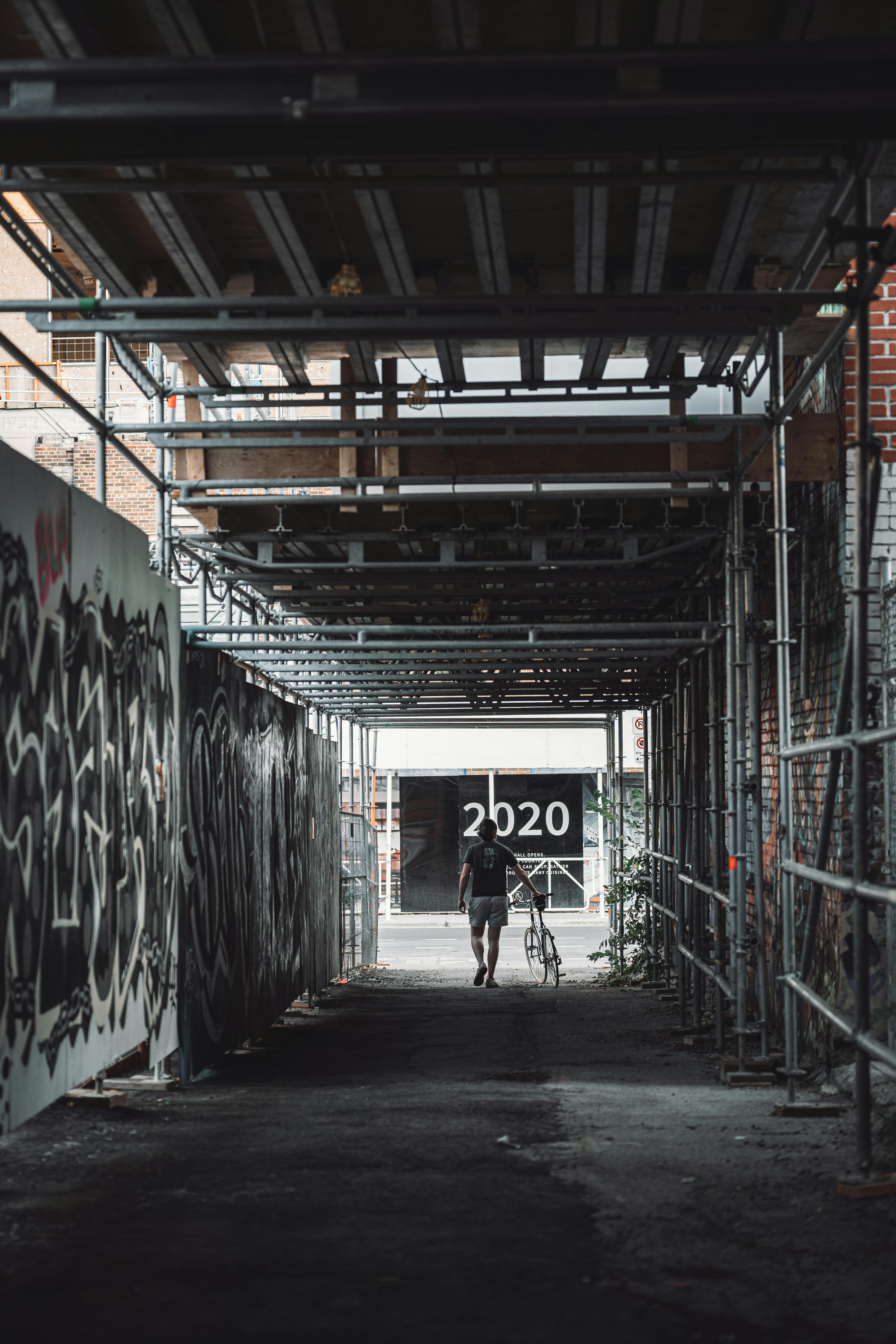 a person walking with his bicycle under a steel scaffolding