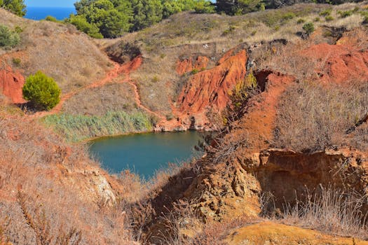 Explore the captivating beauty of the bauxite quarry lake surrounded by rugged, red arid hills under a clear blue sky.