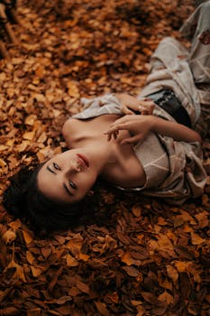 Stylish woman posing gracefully on a bed of autumn leaves, capturing a moment of beauty and fashion.