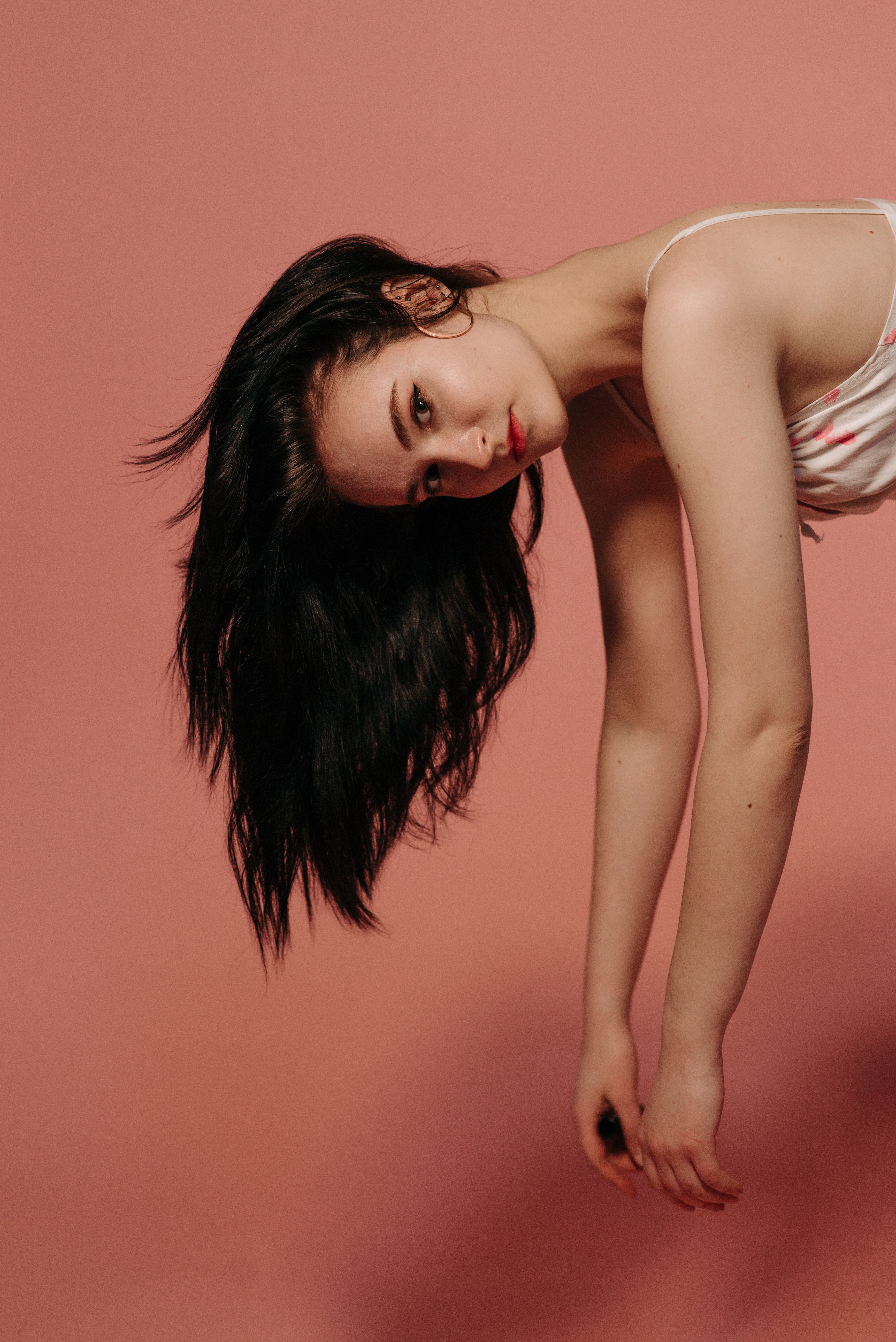 Artistic side-angled portrait of a woman with black hair on a pink background.