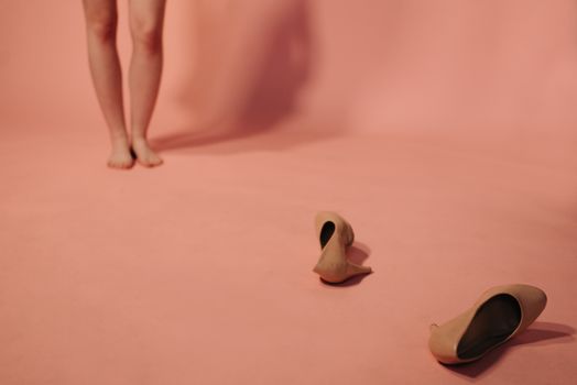 Close-up of bare legs with high heels on a pink studio background.