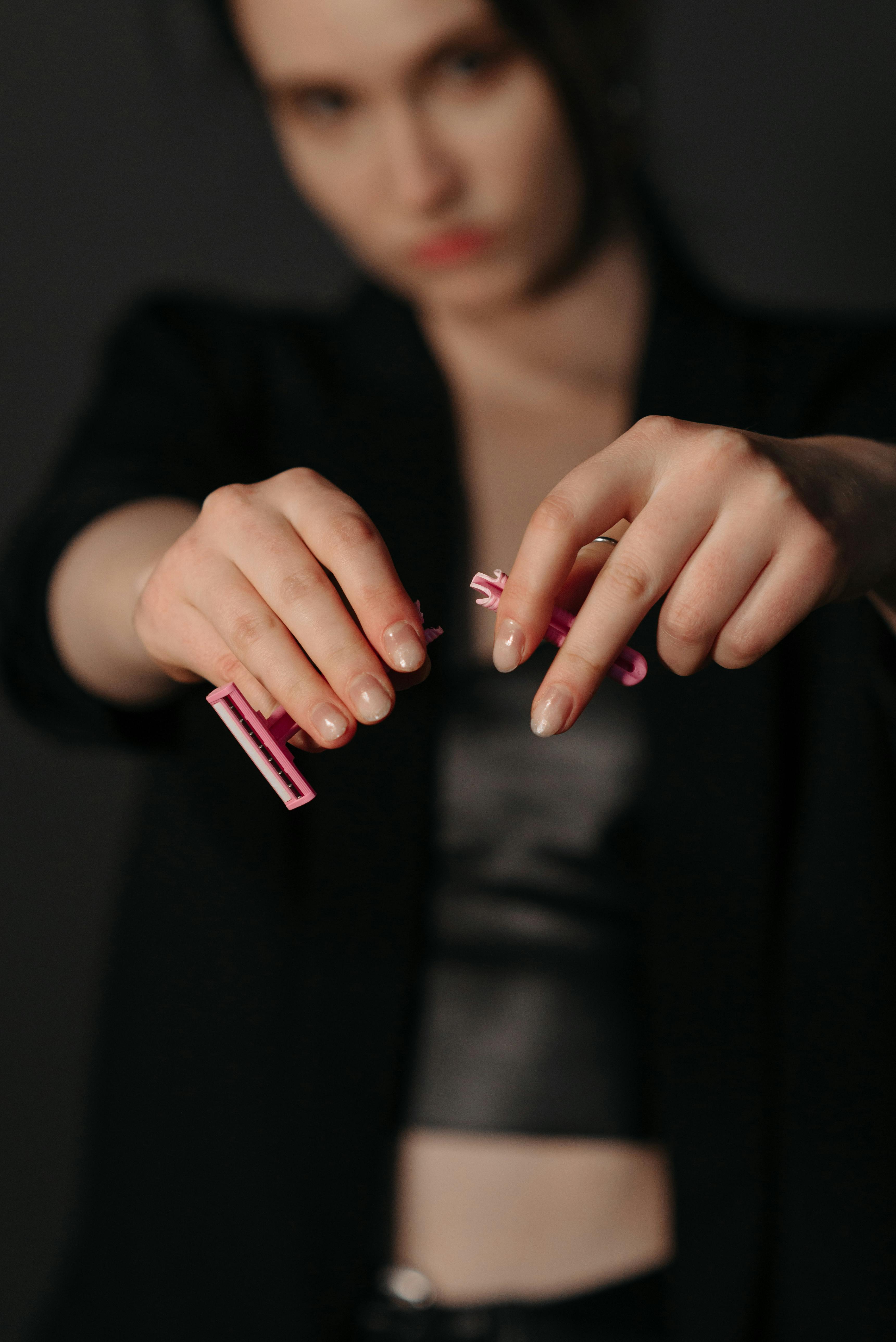 A woman wearing a blazer breaks a pink disposable razor, symbolizing rebellion against beauty norms, with a serious expression.
