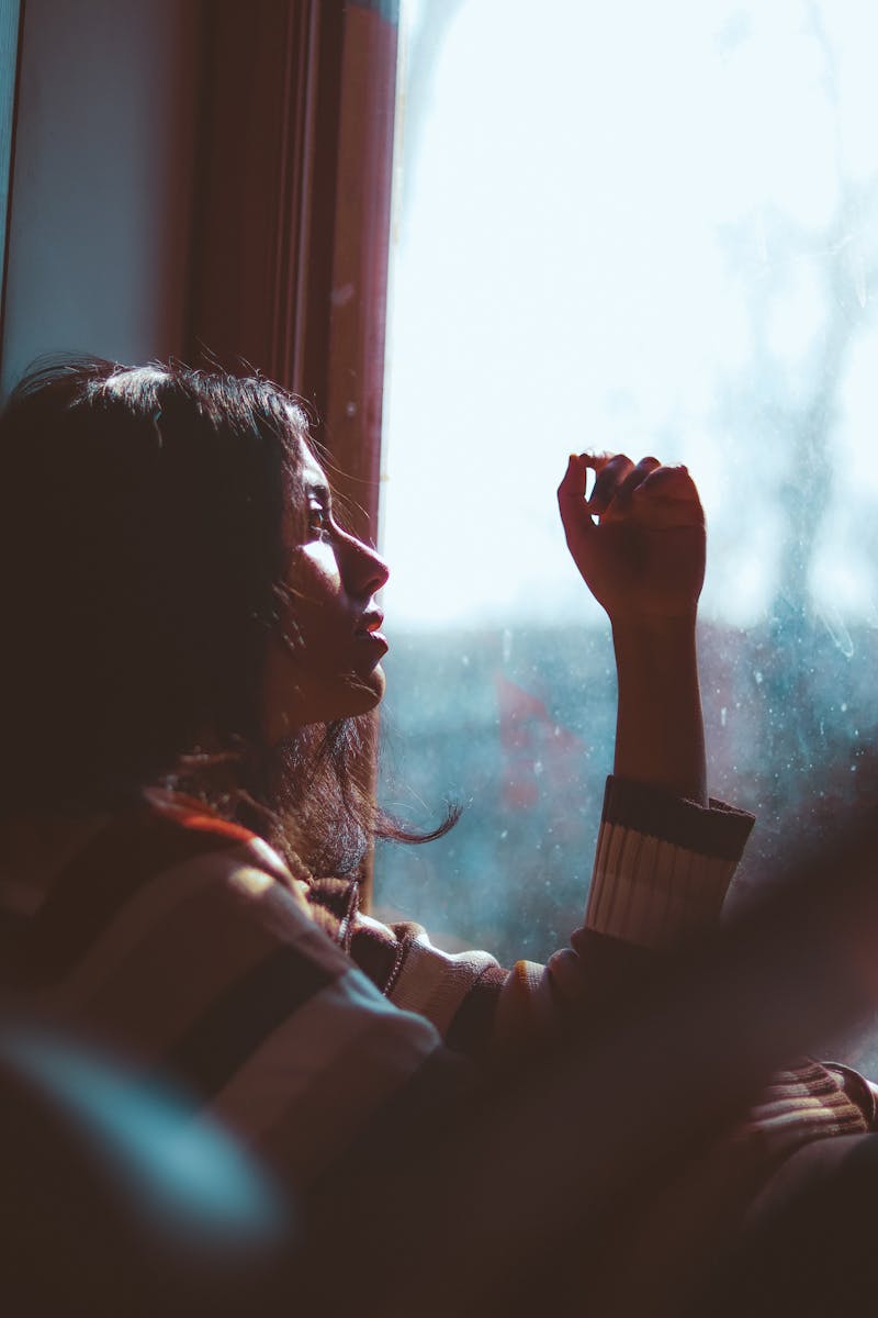 Pessoa tranquila sentada ao lado da janela com luz natural, representando calma e autoconhecimento