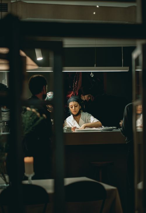 Free A chef preparing dishes at a dimly lit restaurant counter with patrons nearby. Stock Photo