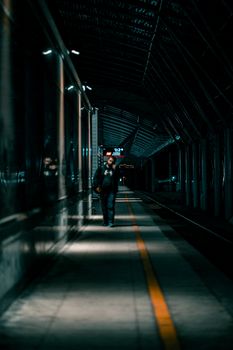 A solitary figure walks along a dark, deserted subway platform at night, creating a moody urban atmosphere.