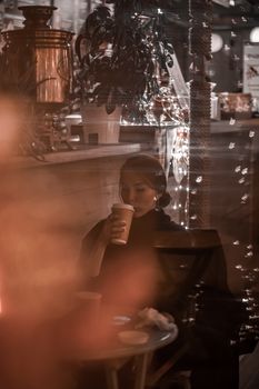 A woman enjoys a warm drink in a cozy, dimly-lit cafe setting.