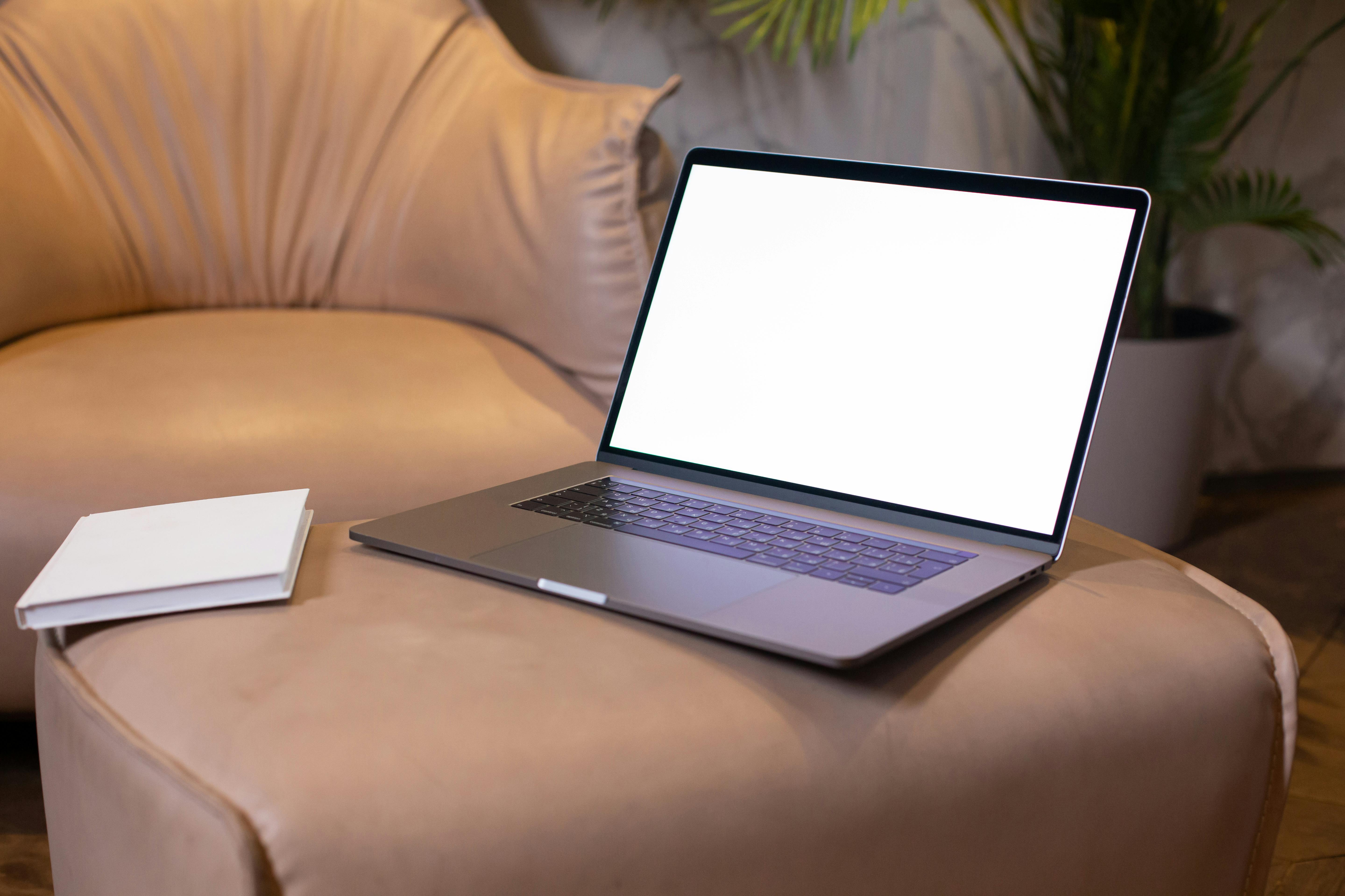 A Laptop and A Book On Beige Leather Sofa