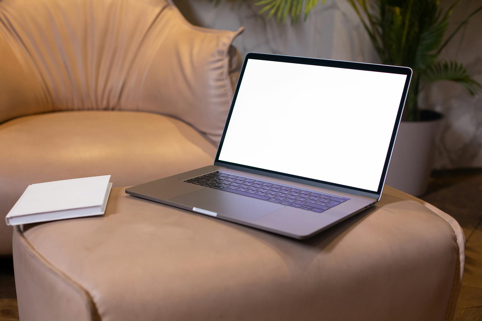 A Laptop and A Book On Beige Leather Sofa